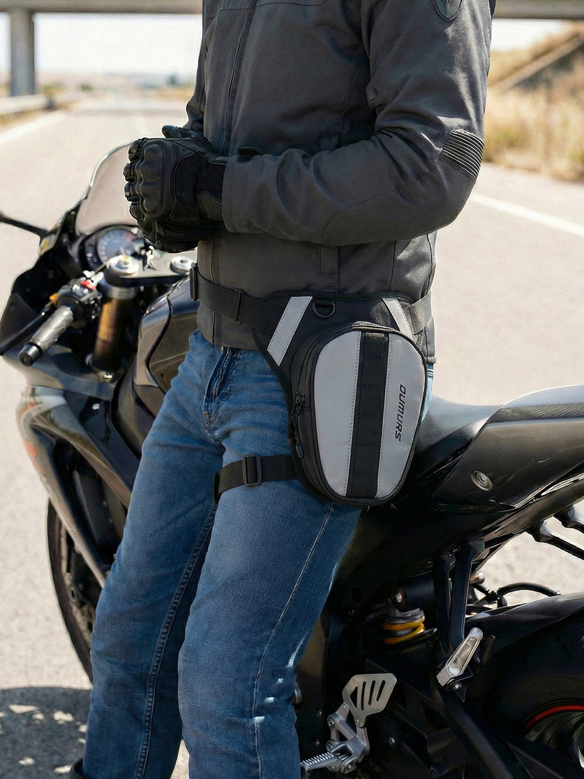 A person wearing a gray motorcycle jacket and blue jeans sits on a black sport motorcycle, wearing a gray and white GORUFOUR side pouch bag around the waist.