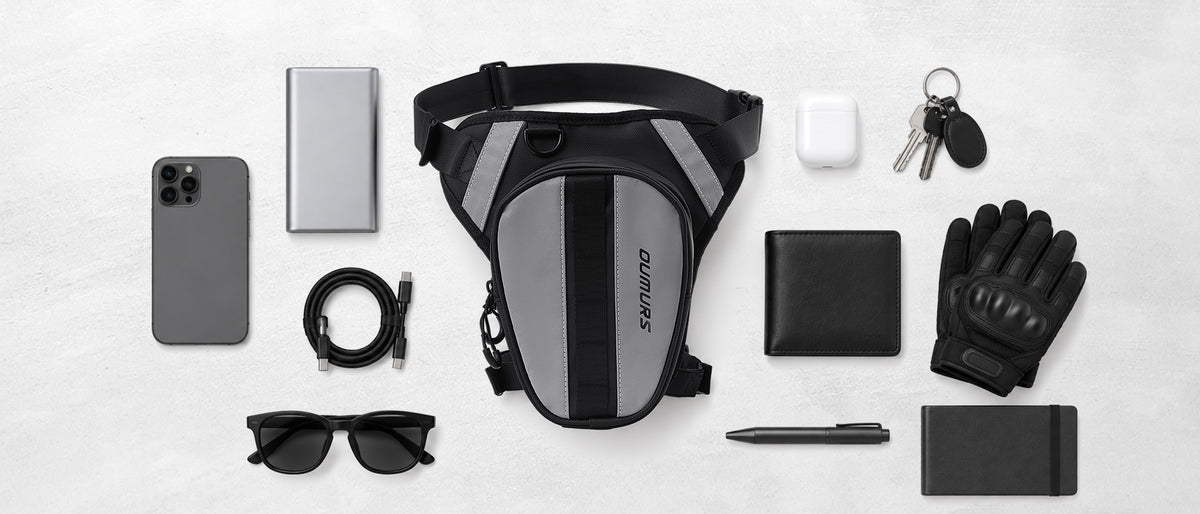Black and gray Oumurs leg bag surrounded by a phone, gloves, keys, wallet, sunglasses and other small essentials.