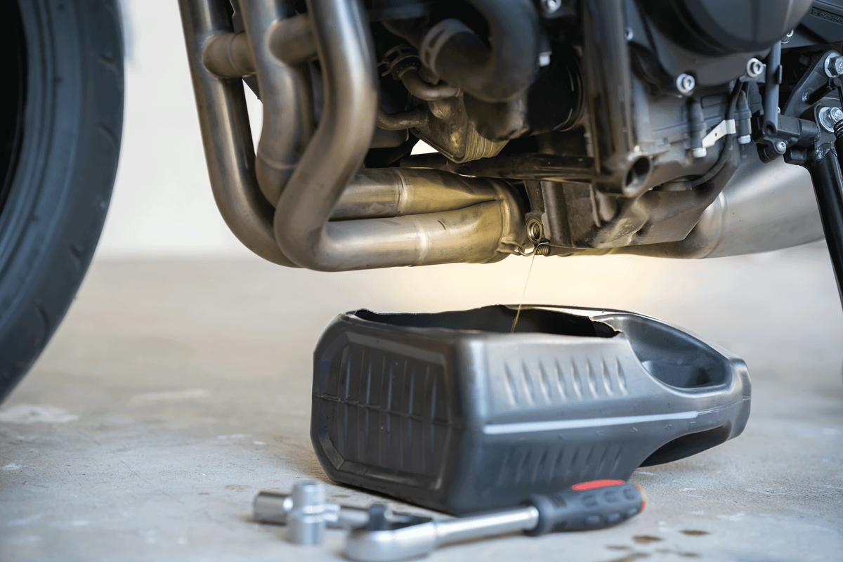 Draining old engine oil from motorcycle into a black drain pan during DIY oil change