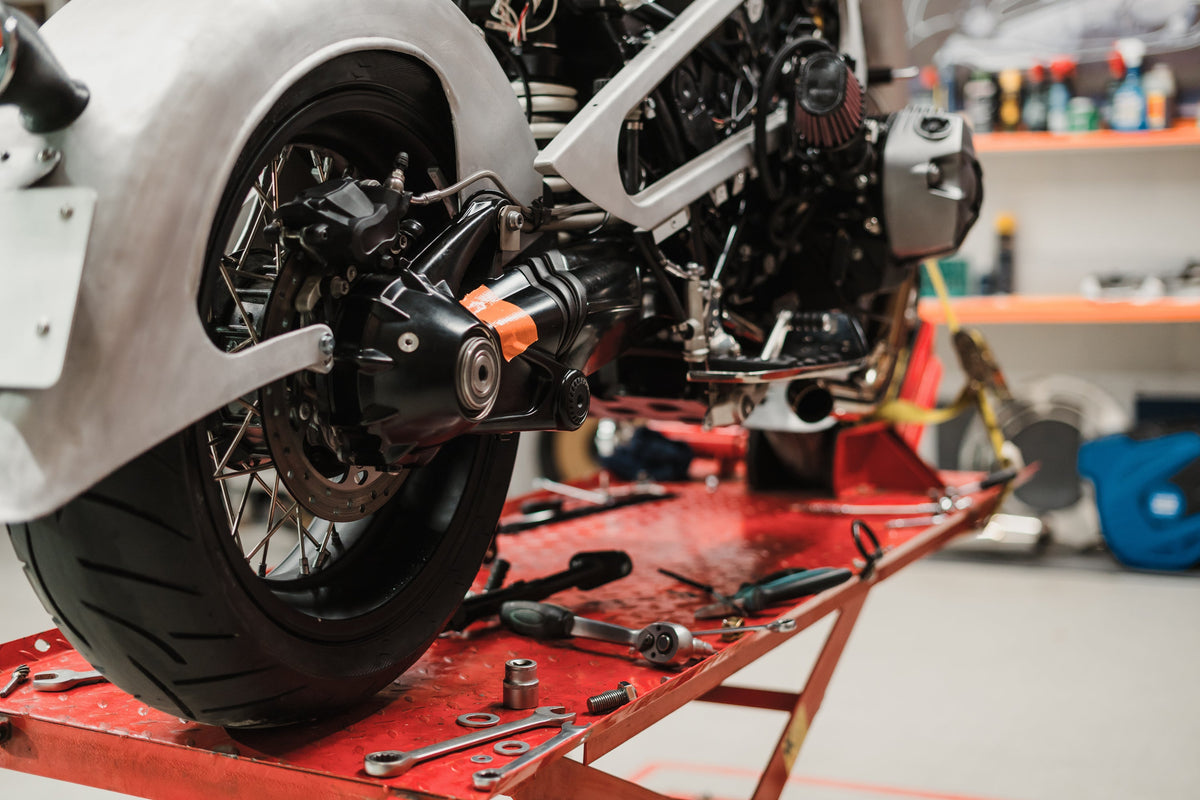 A detailed photograph of a customized motorcycle under repair on a red hydraulic workshop lift.