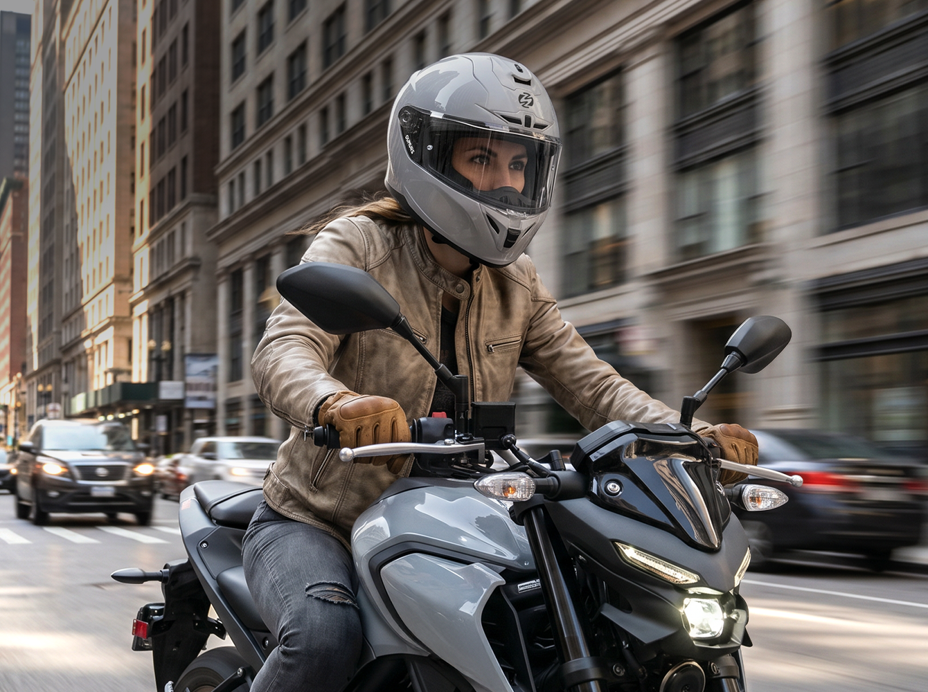 A woman wearing an Oumurs-361S concrete gray full-face helmet rides a gray motorcycle down a city street