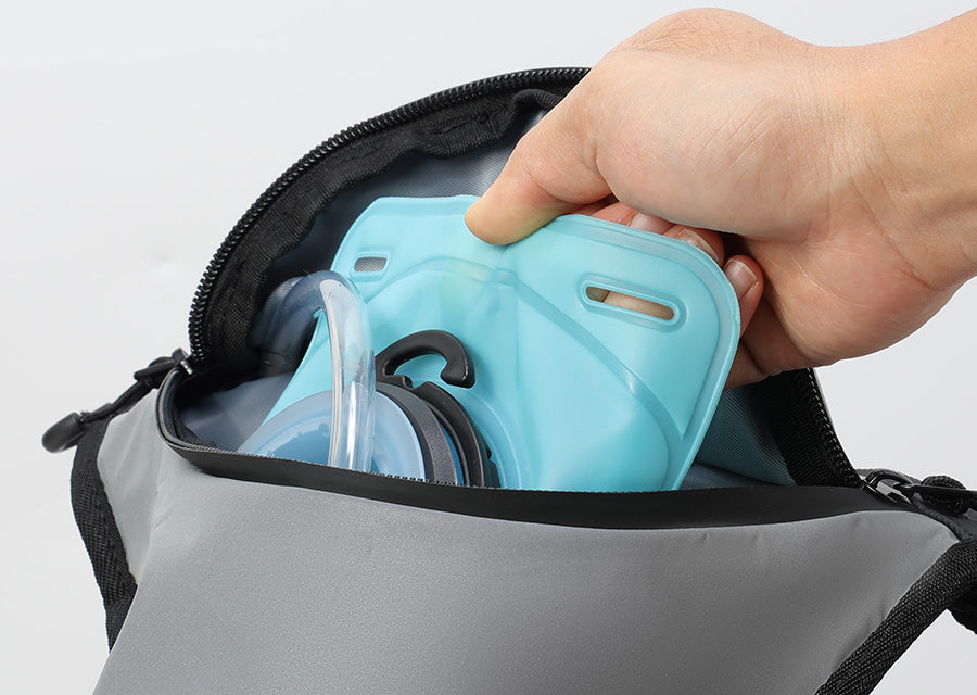 A hand inserting a light blue hydration bladder into a gray and black backpack against a clean white background.