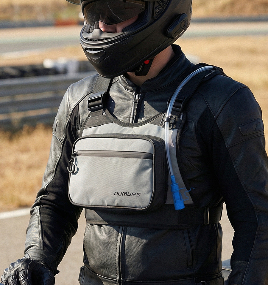 A close-up of a motorcyclist wearing a black leather jacket and helmet, wearing a gray DUMUPS crossbody bag with a black strap and a blue hydration tube.
