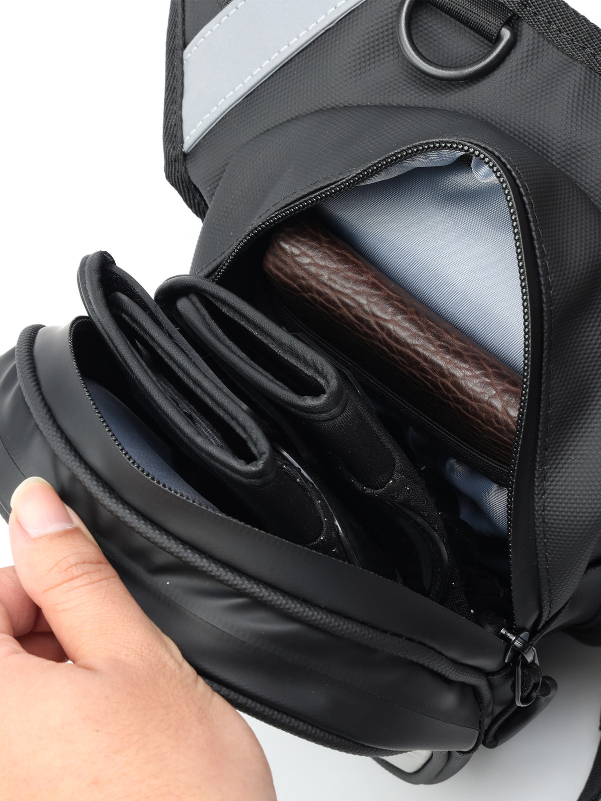 A close-up of a OUMURS_Reflekta_Motorcycle_leg_bag with a hand opening a front zipper compartment, revealing a brown leather item inside, on a white background.