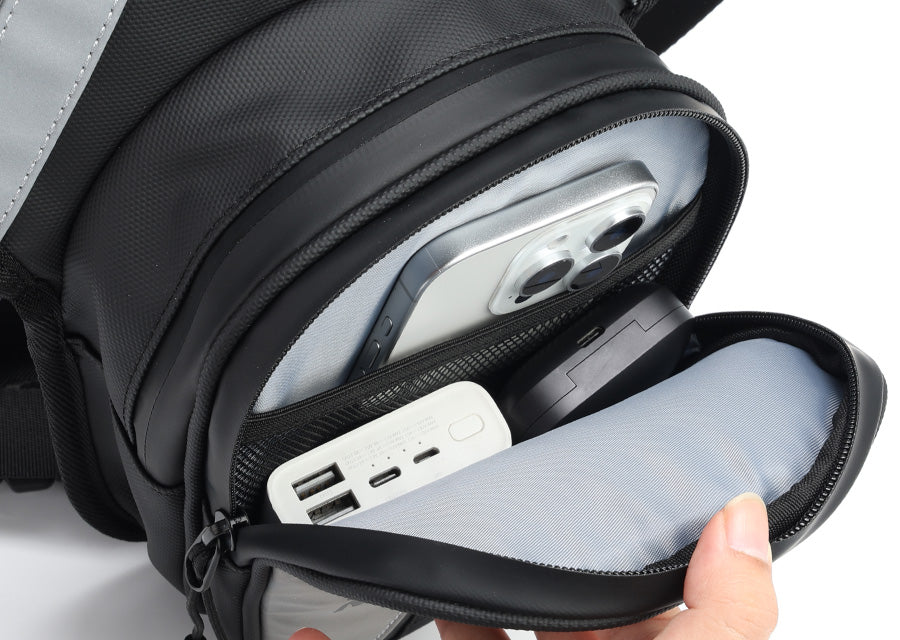 Open front pocket of an Oumurs motorcycle leg bag holding a smartphone, power bank and small accessories.