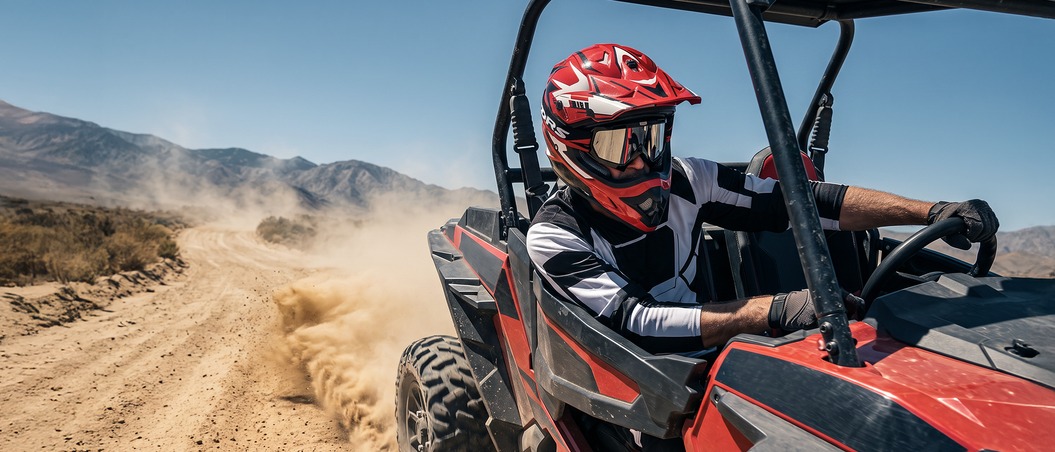 A man wearing an Oumurs 805 Engine Red off-road helmet drives a UTV through desert hills.
