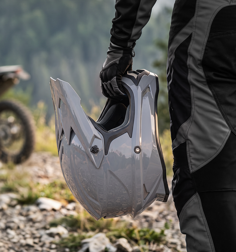 A rider holds the Oumurs 805 gray off-road helmet in one hand while walking on a rocky trail.