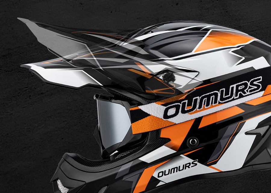Close-up of a motocross helmet in black, white, and orange with a clear visor and silver shield lens, featuring the OUMURS brand name on a dark textured background.