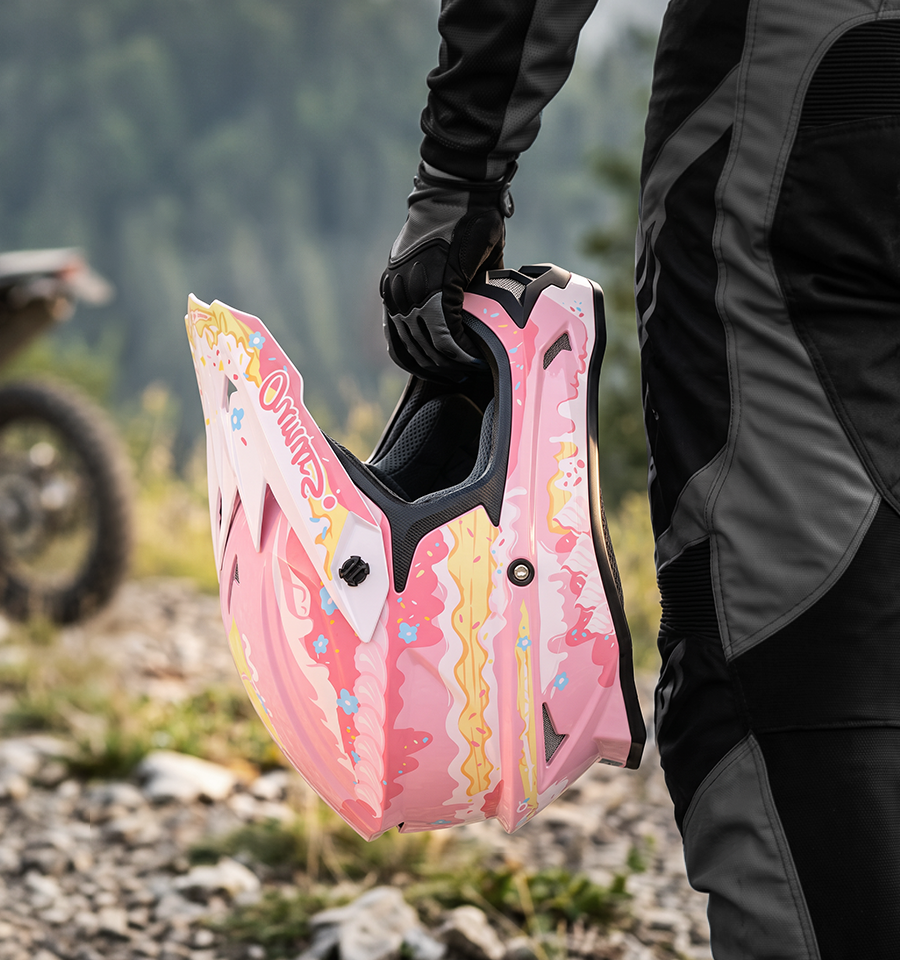 A rider holds the Oumurs 805 Pink off-road helmet in one hand while walking on a rocky trail.