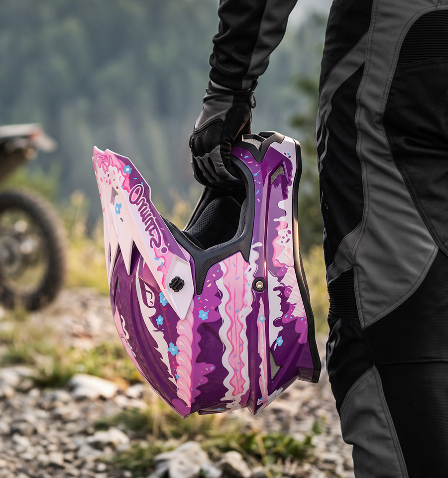 A rider holds the Oumurs 805 Purple off-road helmet in one hand while walking on a rocky trail.