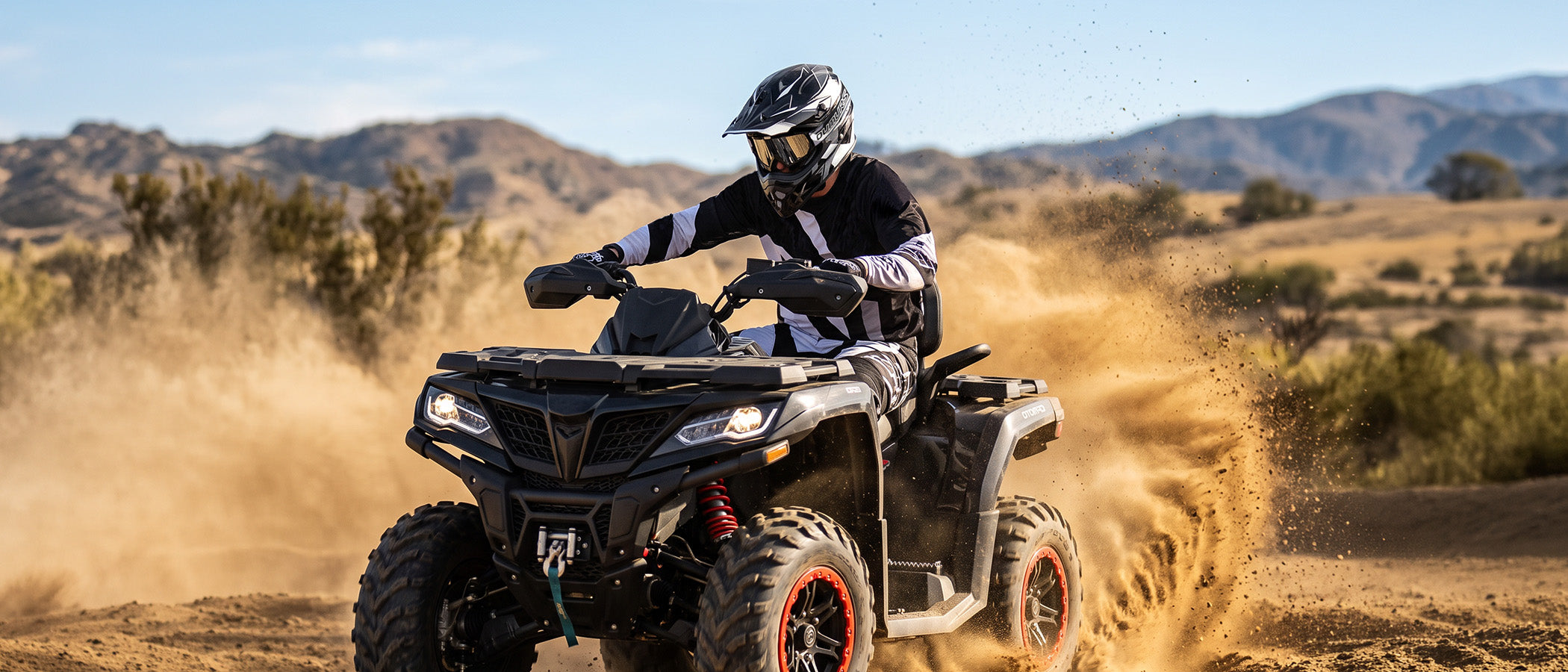 A rider wearing an Oumurs 805 victory gray off-road helmet drives an ATV through the desert and kicks up dust.