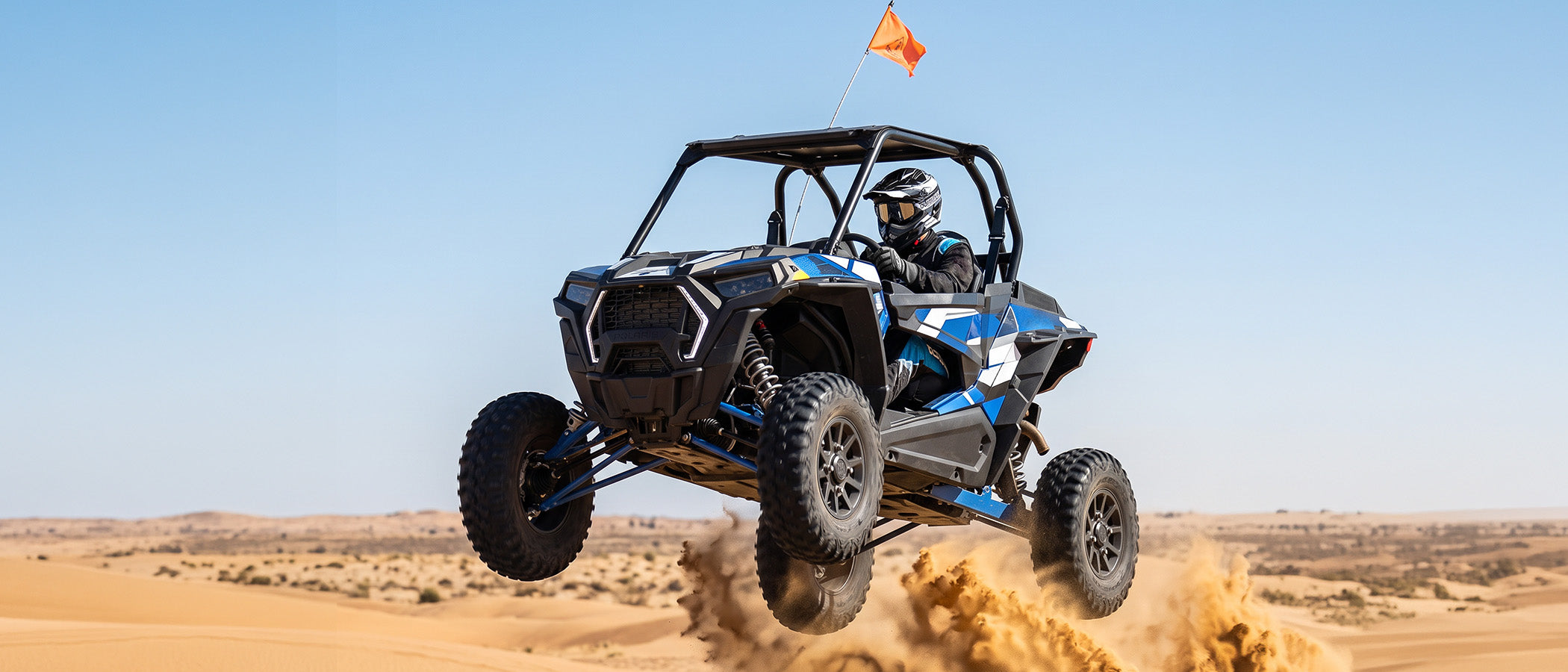 A rider wearing an Oumurs 805 victory gray off-road helmet catches air in a UTV over sand dunes.