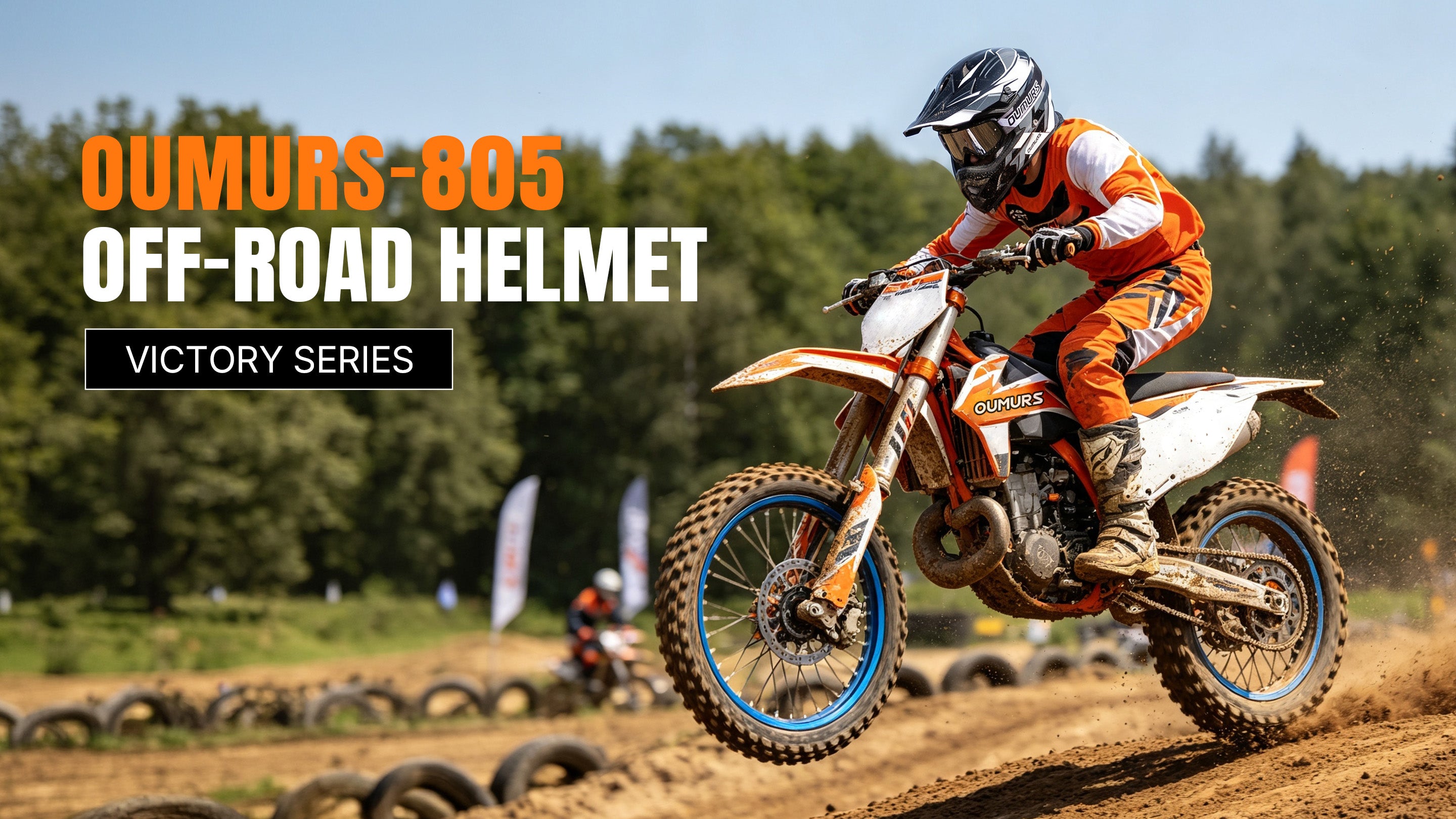 A motocross rider wearing an Oumurs 805 Victory Gray off-road helmet catching air on a dirt bike at a motocross track lined with tire barriers.
