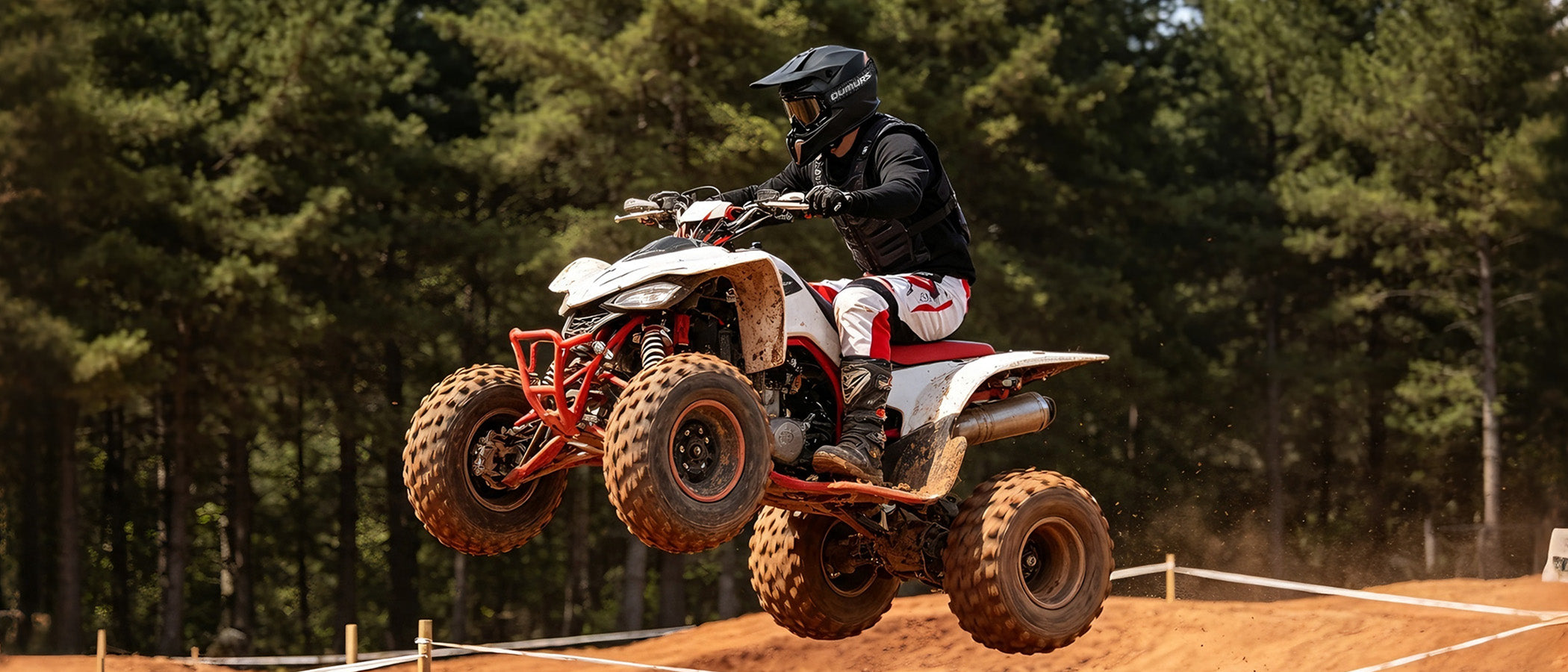 A man wearing an Oumurs 806 Matte Black off-road helmet rides an ATV on an off-road dirt track, with a dense forest in the background.