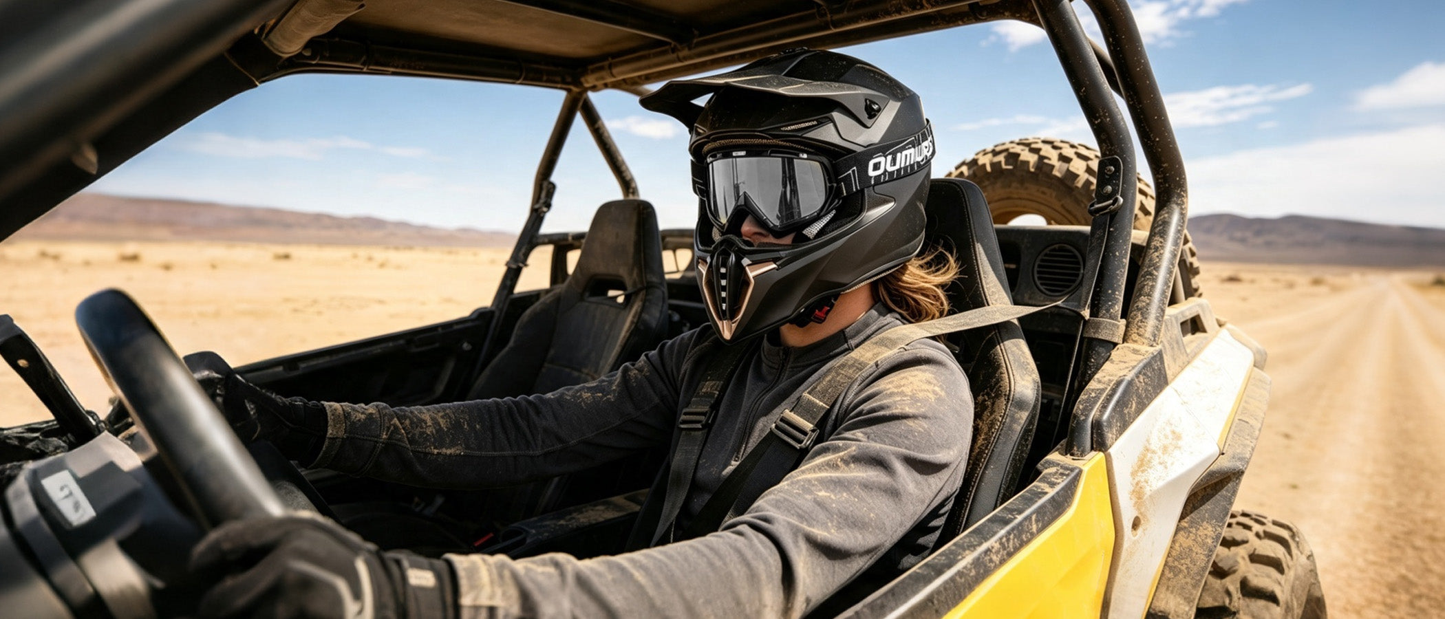 A woman wearing an Oumurs 806 Matte Black off-road helmet with goggles drives a UTV on a desert dirt road.