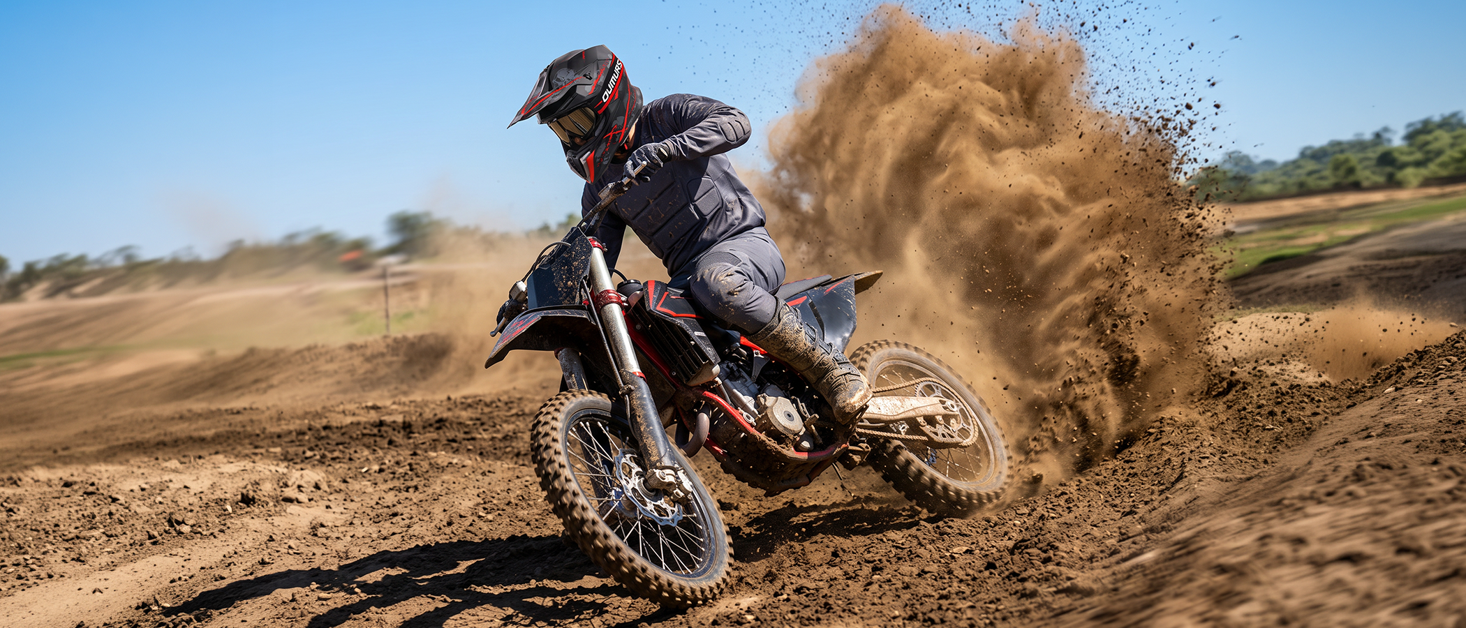 A rider in full protective gear wearing an OUMURS 806 Red Skull motocross helmet leans a red and black dirt bike around a dirt track, kicking up a large cloud of dust.