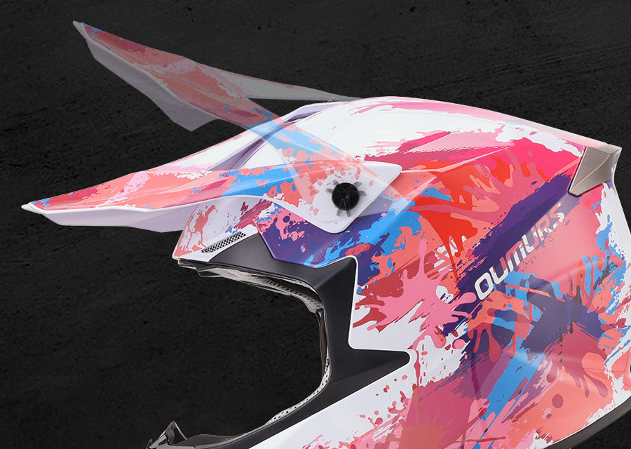 A close-up of a motocross helmet shell featuring a vibrant abstract paint splatter design in pink, blue, and purple over a white base, with the brand name 'QUINUKS' printed on the side.