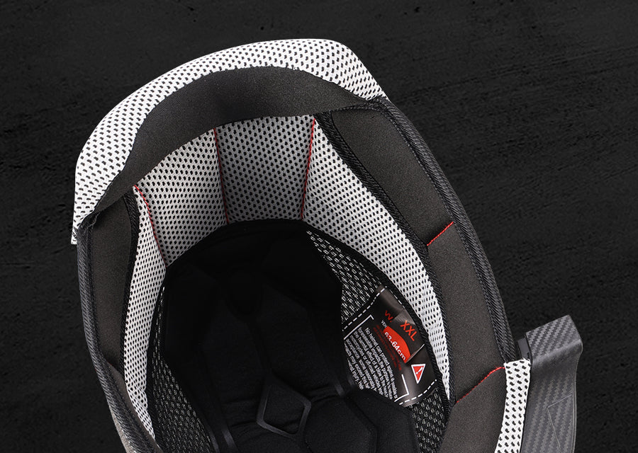 Close-up of a motorcycle helmet interior showing a black and white mesh patterned shell, black foam padding, and red stitching details against a dark textured background.