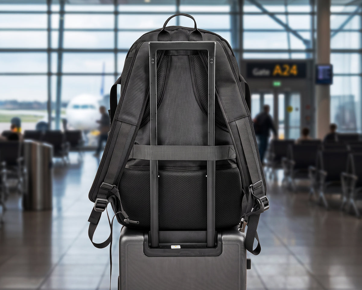 Black OUMURS backpack secured over a rolling suitcase handle with its rear luggage strap.