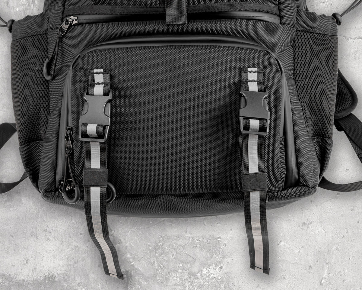 Close-up of reflective strips on the front buckle straps of a black OUMURS motorcycle backpack