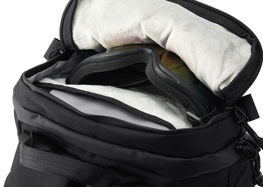 A close-up of a black insulated bag with its zipper open, showing a white fleece lining and a black ski or snowboard goggle resting inside.