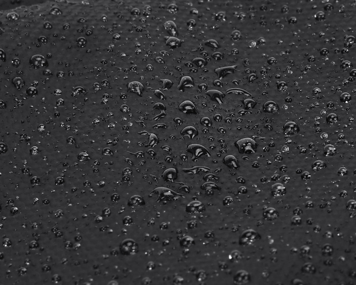 Close-up of a dark1800D Oxford Fabric surface covered with small water droplets, showing glossy reflections and a waterproof or hydrophobic finish.