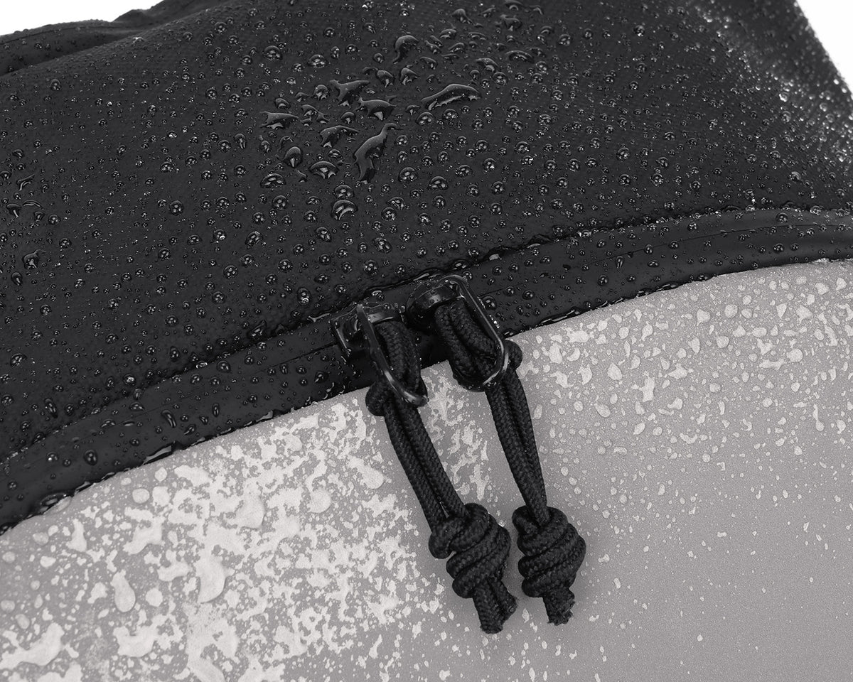 Close-up of a black waterproof fabric with water droplets and a black zipper pull, shown against a light gray water-splattered surface.