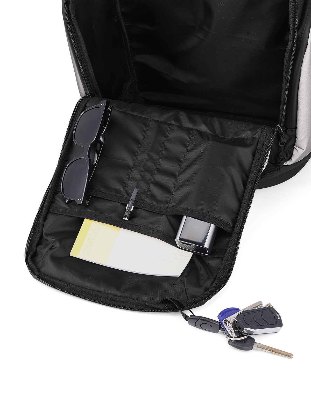 An open black backpack showing its interior organization with a padded compartment holding sunglasses, a card holder, and a small rectangular accessory, plus a key fob and keys resting outside the bag on a white background.