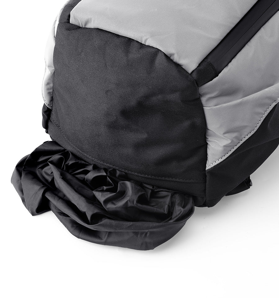 Close-up of a black and gray backpack showing the main body fabric, zipper area, and a black rain cover draped in front on a white background.