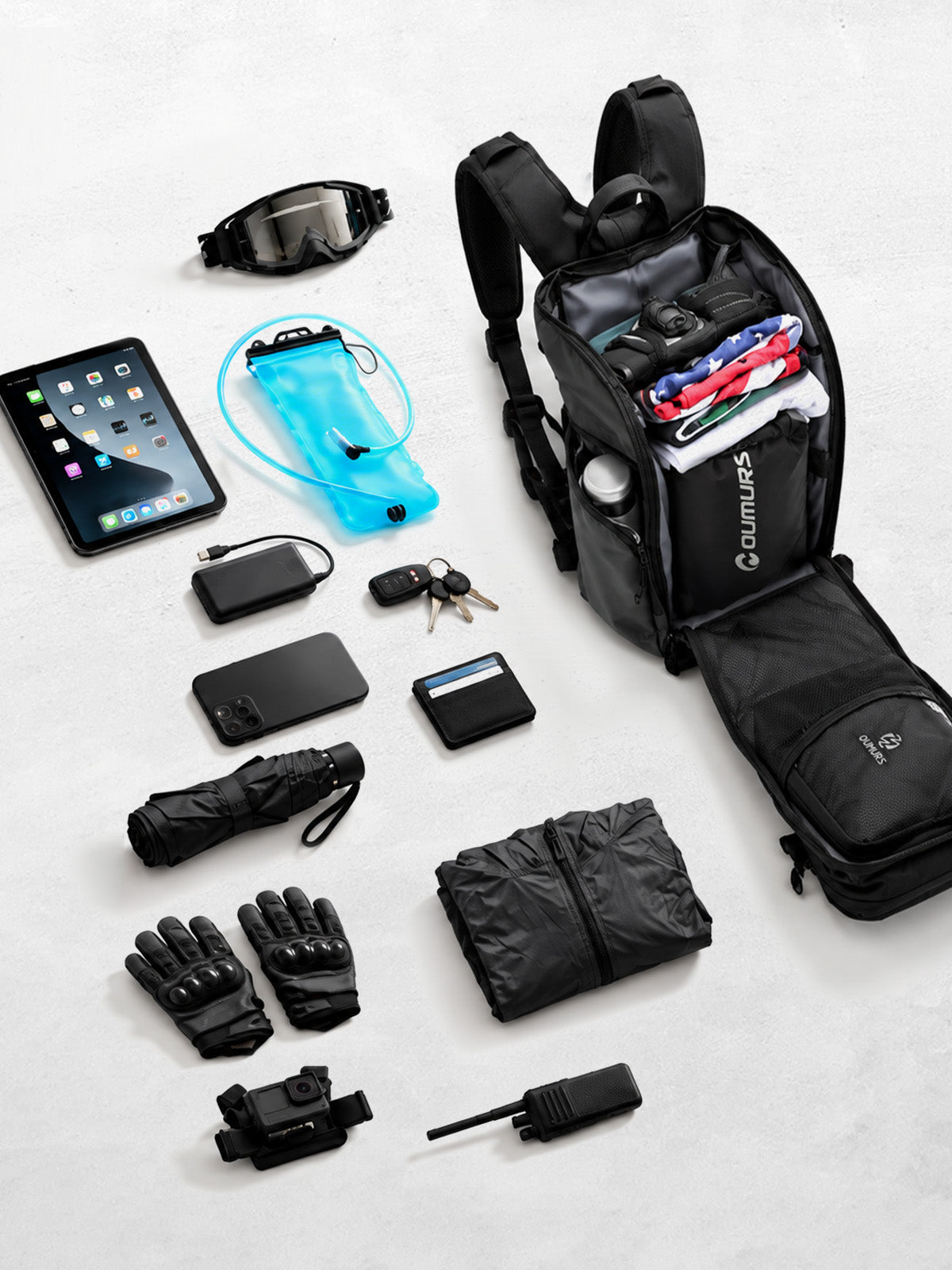 Open Oumurs 15L motorcycle backpack surrounded by riding gear, a hydration bladder, electronics and everyday essentials.